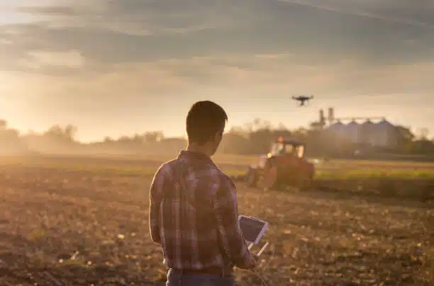 A farmer using a tablet to monitor crop data in a field, with a drone flying overhead - Precision Farming